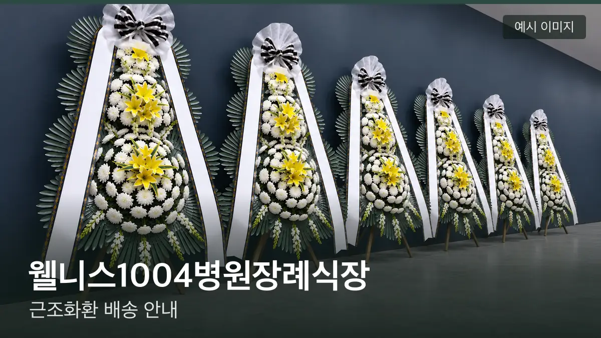 웰니스1004병원장례식장 근조화환 예시 이미지 — 흰 국화 3단 근조화환이 벽을 따라 나란히 놓인 모습